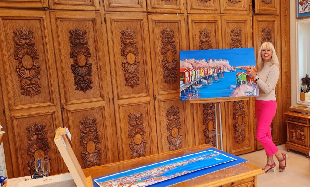 En stor oljemålning på ett staffli i Ariana Ramhages ljusa ateljé i Gråbo, med färgpaletter och penslar i förgrunden.